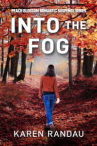 Cover of Christian thriller author Karen Randau's "Into the Fog." A woman with long dark hair, wearing a brown jacket and blue jeans, walks alone down a leaf-covered forest path surrounded by vibrant red and orange autumn trees.