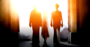 Three silhouetted figures walking down a dark passageway toward a bright glowing light, creating a mood of mystery, faith, and emotional transformation
